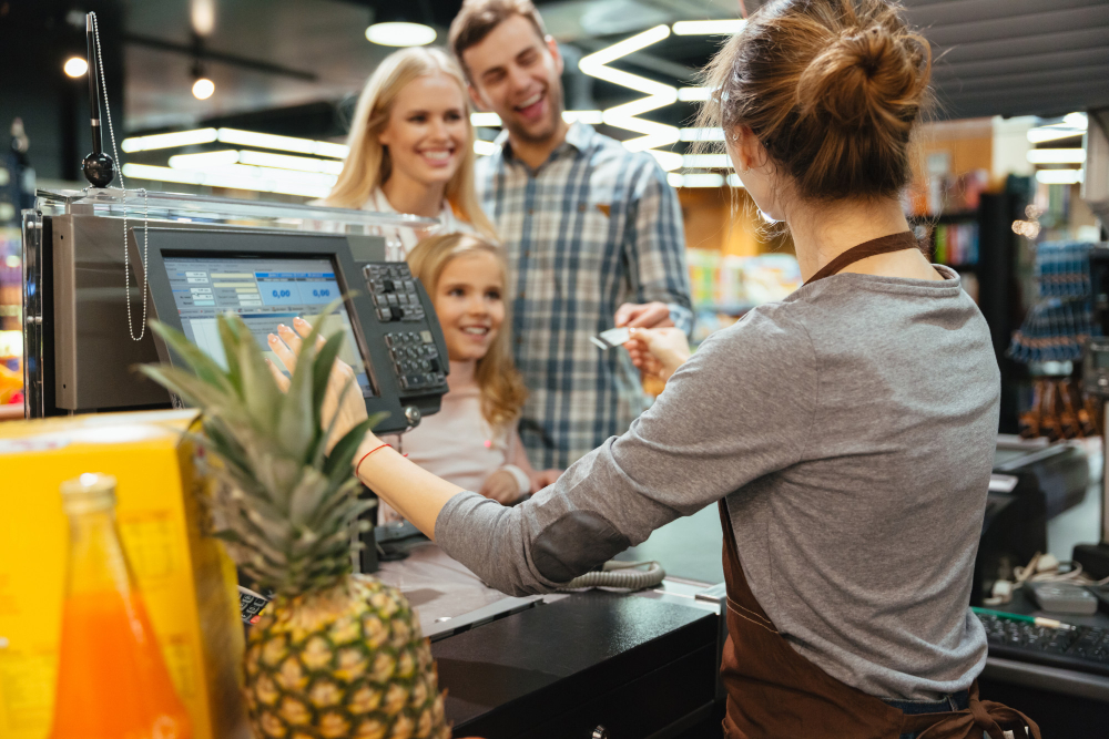 Une famille qui présente à une caissière un bon d'achat, ce qui leur permets de faire des économies sur leurs courses au supermarchés